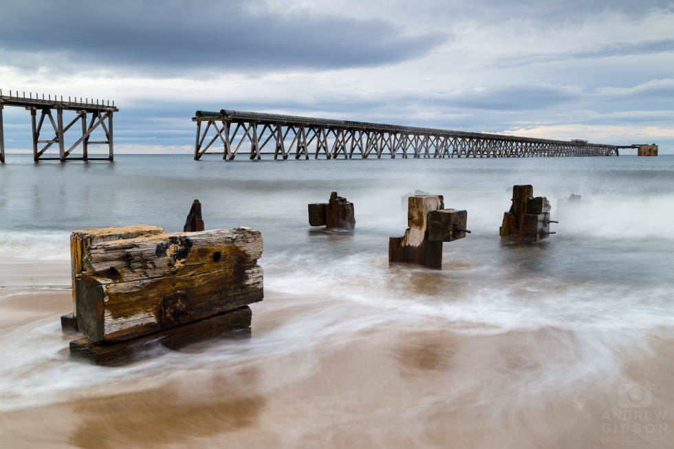 High tide at the derelict industrial pier at Steetley, with softened waves breaking around timbers in the foreground.