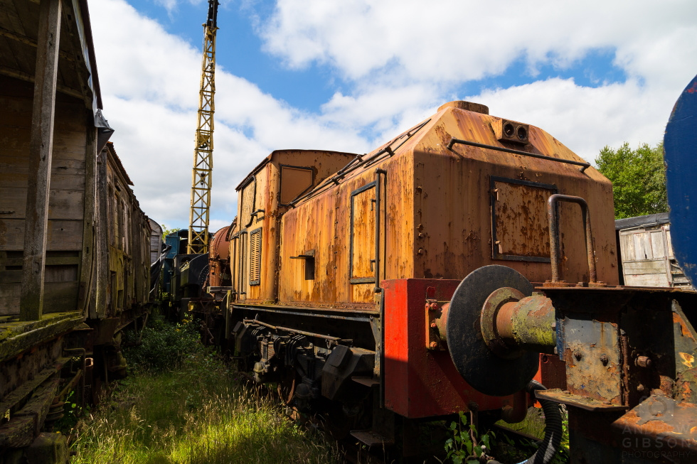 Orange engine surrounded by derelict coaches under a blue sky, at Tanfield Railway Yard.